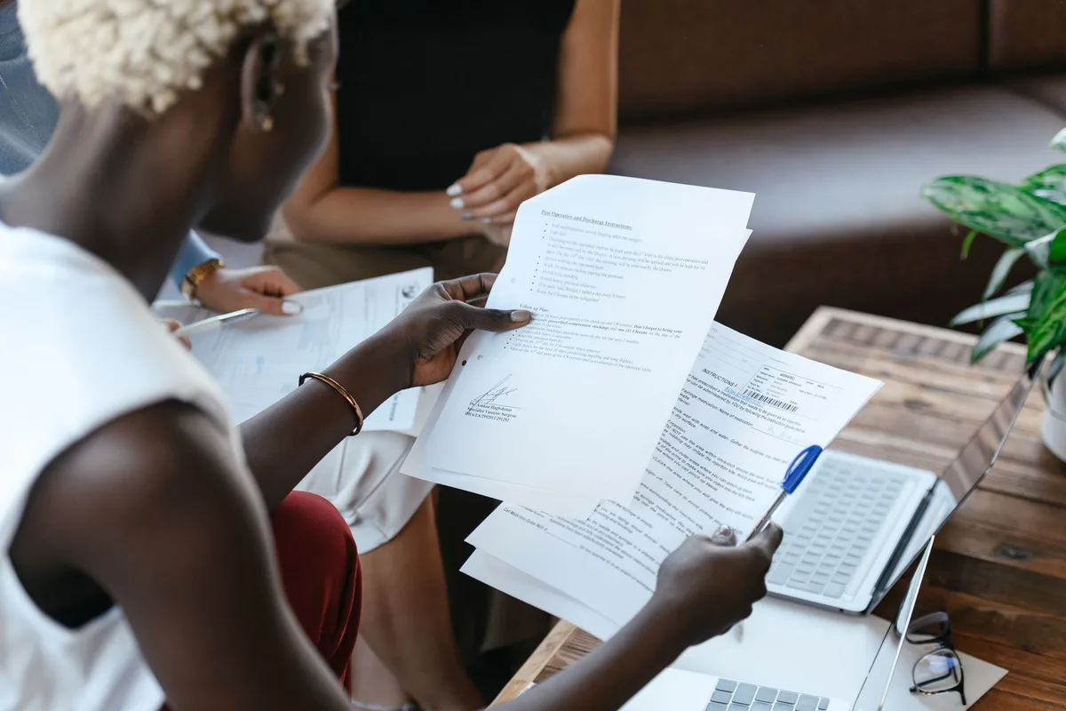 A woman comparing data across two paper documents on a desk, reviewing options side by side