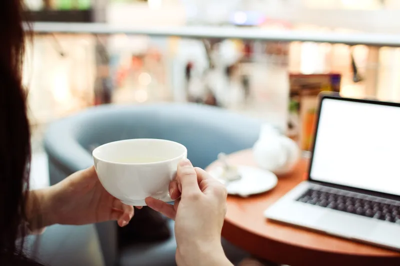 Person relaxing with a cup of coffee next to a laptop, representing the payoff of a follow-up sequence that runs on its own
