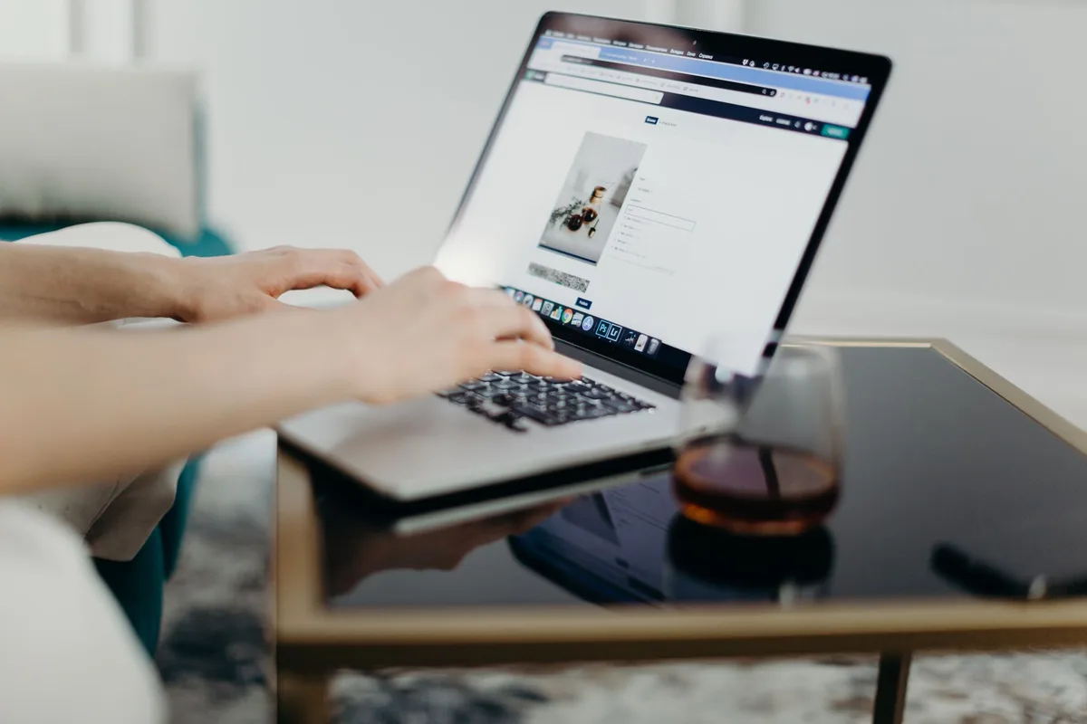 A person working at a desk using a laptop and smartphone, managing social media profiles to promote their content
