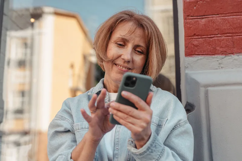 Woman smiling while using her smartphone outdoors, similar to the moment a quiz-taker checks their phone after submitting their email to see their result