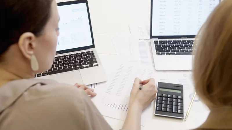 Two people reviewing data and formulas on a laptop screen