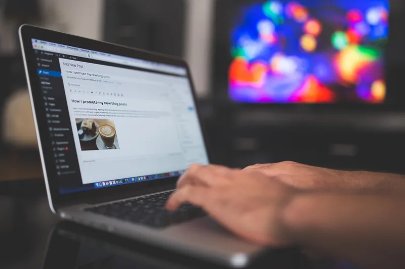 Hands typing on a laptop with a blog post visible on screen, representing content creation and inline opt-in placement