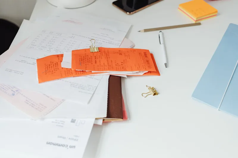 A messy pile of unsorted receipts and papers clipped together on a white desk
