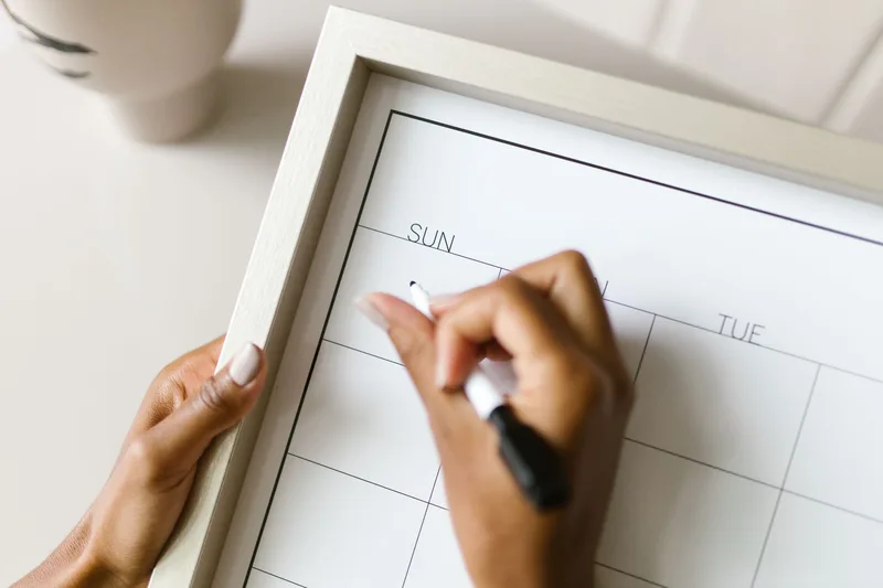 Hands holding a wall calendar and marking a date with a marker pen